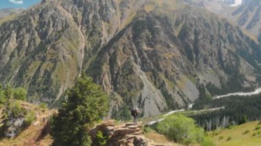 A man shoots a photo in the mountains, he stands on a rock. Great view of the mountain valley