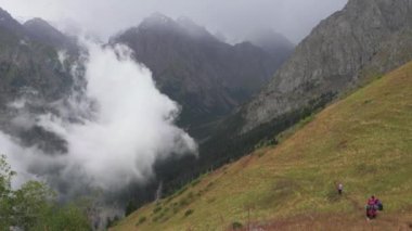 Tourists with backpacks walk along the trail in the mountains. The movement of clouds in a mountain valley. Rainy weather high in the mountains