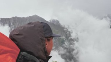 Girl tourist with a backpack high in the mountains watches the weather deteriorate and the movement of clouds. Rainy weather high in the mountains