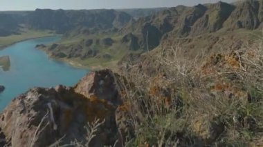 Uçurumun kenarında yürüyen bir adamın bacaklarına yakın çekim. Turkuaz bir nehri olan muhteşem bir kanyon manzarası. İlkbaharda Ili Nehri. Kazakistan. Almaty bölgesi