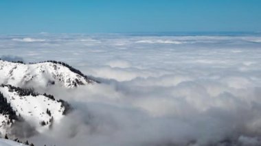 The movement of a dense layer of clouds above the ground. Mountains sprout from the clouds that cover the earth. Timelapse