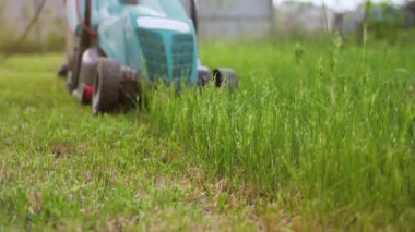 Çim biçme makinesi arka bahçede yeşil çim biçiyor. Yaz ve bahar mevsiminde bahçıvanlık. Ön plandaki çimlere odaklan.