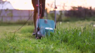 Bir adam arka bahçesinde elektrikli çim biçme makinesiyle çim biçiyor. Yaz ve bahar mevsiminde bahçıvanlık. Ön plandaki çimlere odaklan.