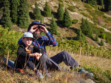 Baba oğul yürüyüşe çıkmışlar. Sakallı bir adam dürbünle bakar. Aile zamanı dışarıda.