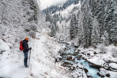 Bir adam kışın karlı bir dağ geçidinde yürür. Nehirle kaplı karlı dağ geçidi