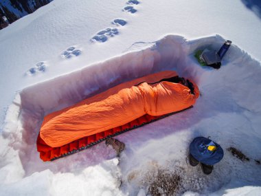 Bir adam karlı bir barınakta uyku tulumunda uyuyor. Kışın dağlarda çoklu gün yürüyüşleri. Dağlarda kış mevsimi