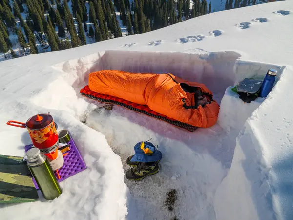 A man sleeps in a sleeping bag in a snowy shelter. Multi-day hikes in the mountains in winter. Winter survival in the mountains