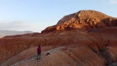 Bir fotoğrafçı sabahın erken saatlerinde alışılmadık kırmızı kayaların fotoğrafını çeker. Kırmızı ceketli, tripodunda kamera olan bir adam. Kum taşı kırmızısı kayalıkları