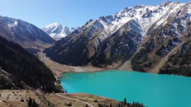 Sonbaharda Büyük Almaty Gölü. Dağlarda İHA uçuşu. Turkuaz dağ gölünün berrak suları ve karla kaplı dağlar.