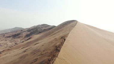 Bir turist büyük bir kum tepesinin tepesine tırmanır. Çöl arazisi. Bir İHA 'dan alınan hava görüntüsü. Şarkı söyleyen kumul. Altyn-Emel Milli Parkı