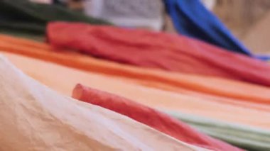 Doğu Caddesi 'ndeki bir pazarda kumaş satarken çekilmiş dikey video görüntüleri. Alıcılar renkli ipek kumaşlara bakıyor.