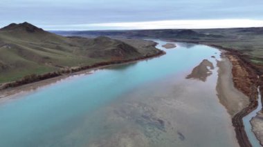Bulutlu bir bahar sabahı nehrin üzerinde uçmak. Kayalık tepelerin arasında turkuaz suyu olan sığ bir nehir. Ili Nehri, Kazakistan
