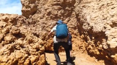 Baba ve oğul, kumtaşı kayalıkları arasında alışılmadık bir doğal ortamda yürüyorlar. Arkadan bak. Sarı kumtaşı kayaları olan terk edilmiş bir bölge. Aile gezisi. Boguty Dağları. Kazakistan. 2x ağır çekim