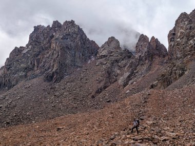 Dağların tepesinde, zaptedilemez kayaların arka planında gezen bir gezgin. Dağlarda, kayaların ve taşların arasında yükseğe tırmanıyorlar. Dağlarda gezmek