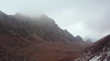 Foggy weather on the Talgar Pass in summer. Flight in the area of Bogdanovich glacier. Bare rocks high in the mountains, lack of vegetation