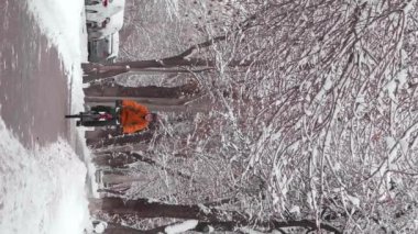 Şehrin kaldırımında bisiklet süren bir adamın dikey video görüntüleri. Adam turuncu bir ceket giyiyor ve kafasında bir kask var. Kentte ekolojik ulaşım