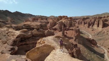 Bir gezgin sıradışı kumtaşı kayalıkları boyunca yürür. Bir turist eşsiz bir dağlık alanda yürüyüş yapıyor. Charyn Kanyonu