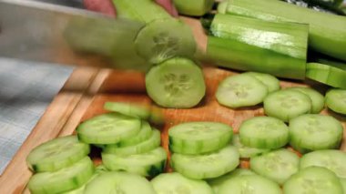 man with chef's knife slicing a cucumber on wooden board