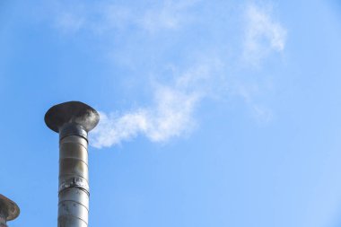 Metalik bacadan mavi gökyüzüne doğru yükselen duman