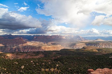 Zion Ulusal Parkı 'nın uzak dağları alçak bulutlar ve mavi gökyüzüne karşı yağan yağmurlu vadiyi çevreleyen geniş bir manzara..