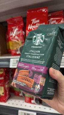 Tim Hortons 'un kahve poşetinin önünde Starbucks kahve çekirdeğini tutan bir el.