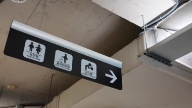 Tavanda asılı duran yön işareti ve tuvalet logosu.