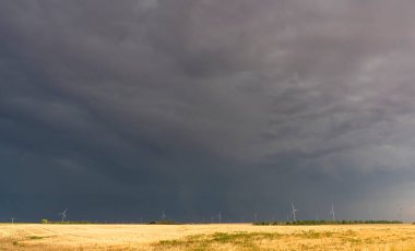 Uğursuz kara bulutlar bir rüzgâr çiftliği ve buğday tarlası üzerinde toplanarak yaklaşan fırtınayı vaat ediyor.