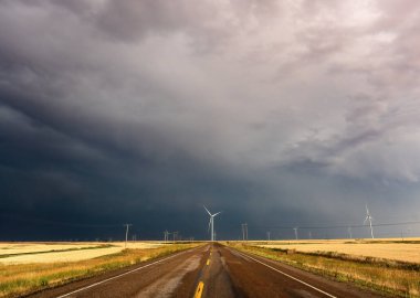 Uğursuz kara bulutlar bir rüzgar türbini çiftliği ve bir kır yolu üzerinde toplanıyor.