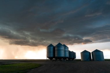 Gün batımında tahıl ambarları üzerinde oluşan uğursuz fırtına bulutları kırsal alanda dramatik ve güçlü bir sahne yaratıyor.
