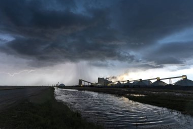 Lightning illuminates potash mine during dramatic storm at sunset clipart