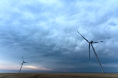 Rüzgar türbinleri hava karardığında dramatik bulutlu bir gökyüzünün altında temiz enerji üretir.