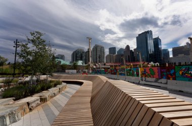 Modern wooden walkway in a park overlooking the skyline of calgary, alberta, canada, under a cloudy sky clipart