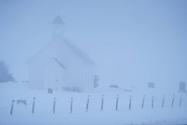 Sis örtüsü soğuk, karlı bir kış gününde küçük bir kilise ve mezarlığı gizler.
