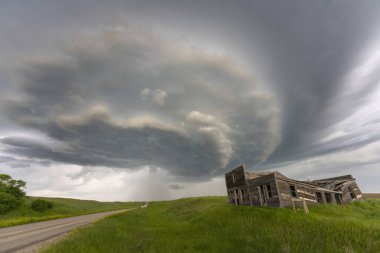 Çayırlardaki terk edilmiş bir ahşap bina ve asfalt yol üzerinde dramatik bir süper hücre fırtınası bulutu oluşuyor.