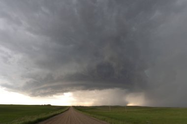 Toprak bir yol ve yeşil tarlalar üzerinde beliren dramatik süper hücre fırtınası doğanın gücünü gösteriyor.