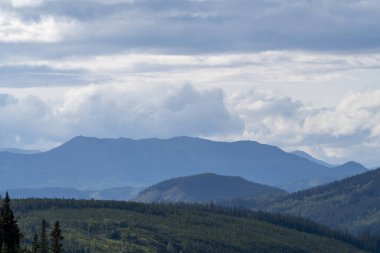 Bulutlu bir gökyüzünün altında ormanla kaplı bir dağ sırasının çarpıcı manzarası.