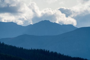 Sakin bir ormanın üzerinde yükselen dağ zirvelerinin çarpıcı manzarası doğanın görkemli manzarasını yaratıyor.