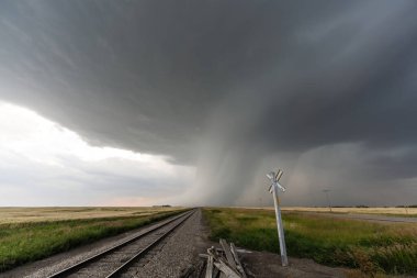 Demiryolu rayları ve kırsal arazi üzerinde şiddetli bir fırtına kopuyor ve yaklaşan havanın dramatik bir sahnesini oluşturuyor.