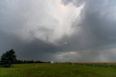 Küçük bir kilise ve kırsal bölgedeki yeşil tarlalar üzerinde kara fırtına bulutları toplanıyor.