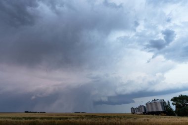 Kara fırtına bulutları kırsal Saskatchewan, Kanada 'da buğday ve tahıl varilleri üzerinde toplanıyor.