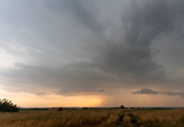 Gün batımında sakin bir alanda toplanan kara fırtına bulutları dramatik bir kontrast yaratıyor.