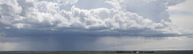 Uğursuz kara bulutlar engin bir tarım arazisinin üzerinde toplanıyor. Uzaktan yağan yağmur dramatik ve karamsar bir atmosfer yaratıyor.