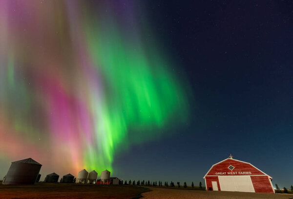 Aurora borealis glowing over great west farms and grain bins in the canadian prairies at night