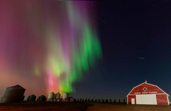 Vibrant northern lights dancing over a farm in the canadian prairies