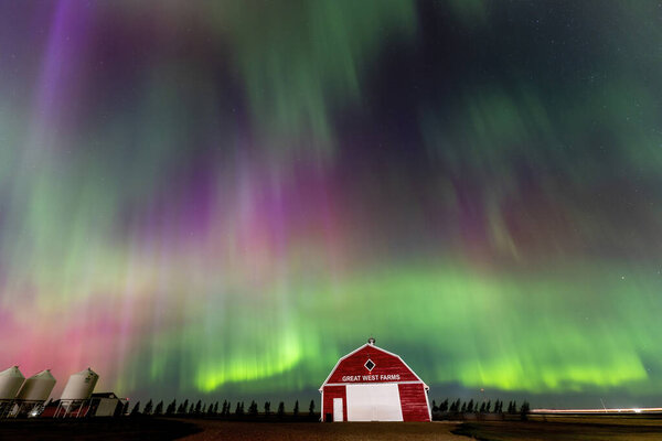 Vibrant aurora borealis illuminating a red barn in a starry night