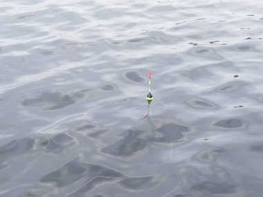 Fishing float in blue water background. Fishing concept. Float in the river water close-up. Fishing in the lake with float