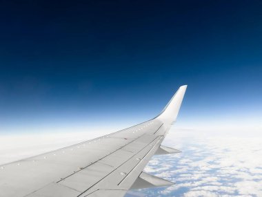 White wing from airplane window on sunny day. Great views of landscape. Aerial view of clouds through a plane window. Wing of airplane with blue sky and beauty clouds
