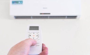 Hand with remote control directed on air conditioner. Climate control indoor concept