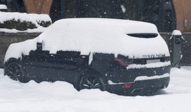 Car under snow in winter. Parked cars and the road are covered with smooth layer of snow. Car covered with snow after a snowfall