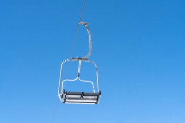 Ski chair lift over blue sky. Ski lift empty ropeway on hilghland mountain winter. Ski chairlift cable way with people enjoy skiing and snowboarding